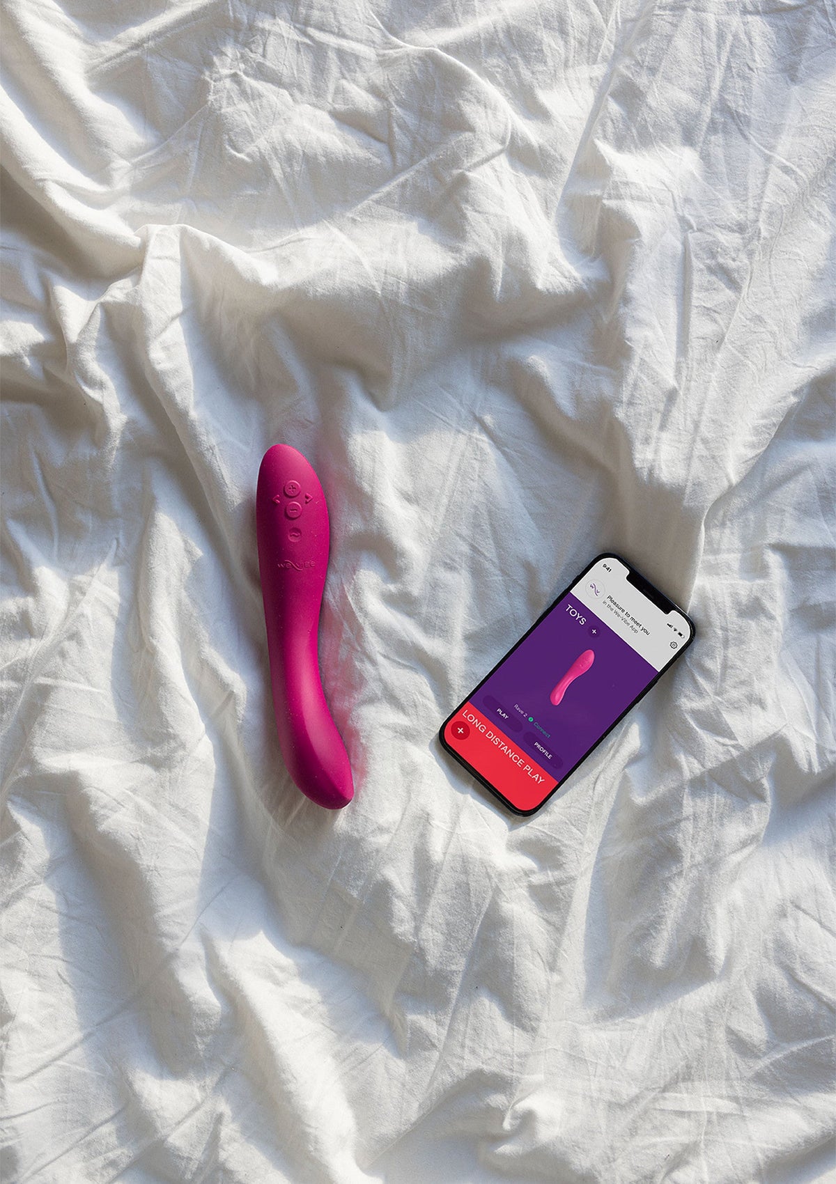 Vibromasseur rose et smartphone sur drap blanc pour le plaisir personnel. Découvrez notre collection!; Roze vibrator en smartphone op wit laken voor persoonlijk plezier. Ontdek onze collectie!; Pink vibrator and smartphone on white sheet for personal pleasure. Discover our collection!