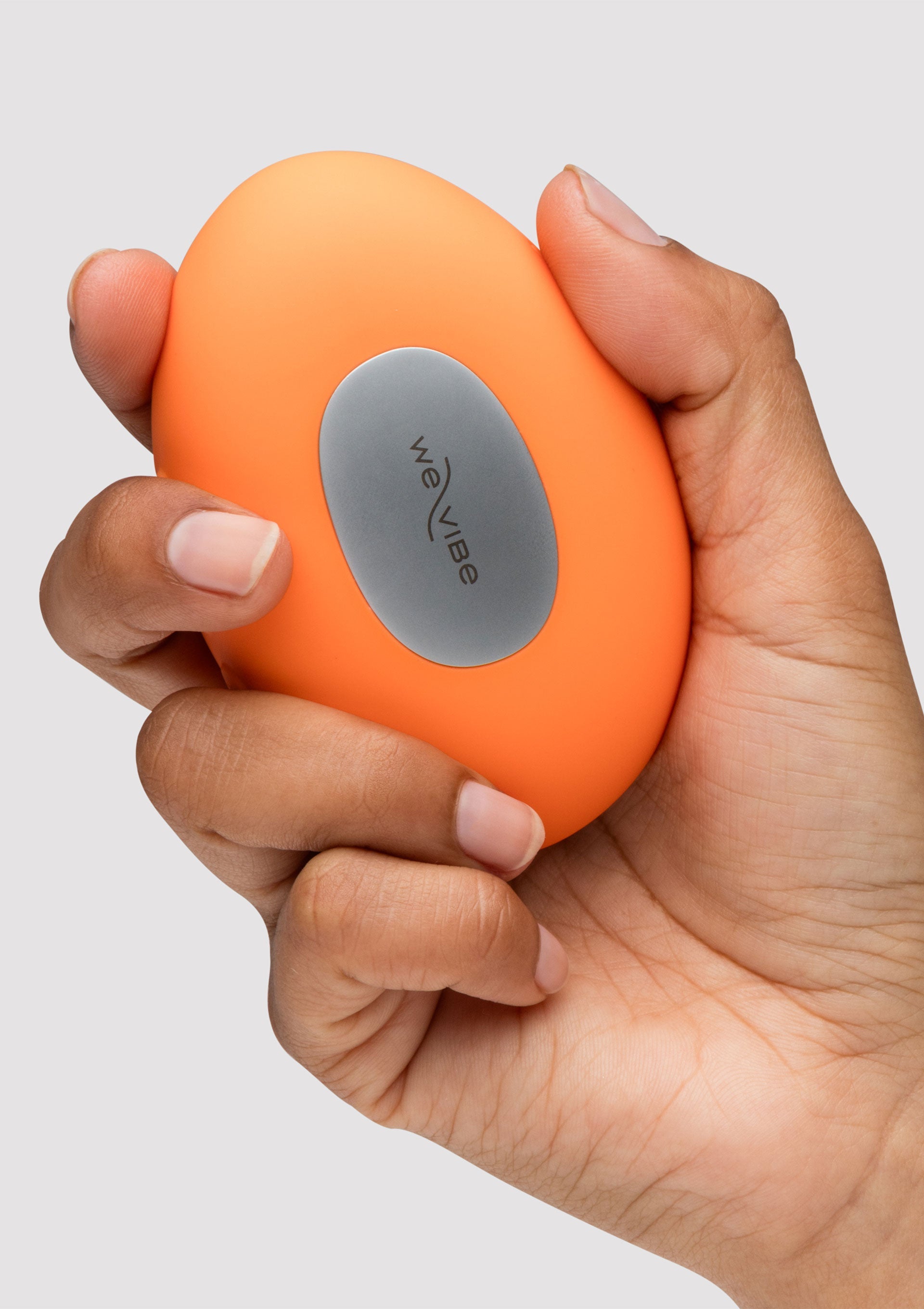 We-Vibe Tango X en orange dans une main. Jouet vibrant compact et puissant.; We-Vibe Tango X in oranje in een hand. Compact en krachtig vibrerend speeltje.; We-Vibe Tango X in orange in a hand. Compact and powerful vibrating toy.