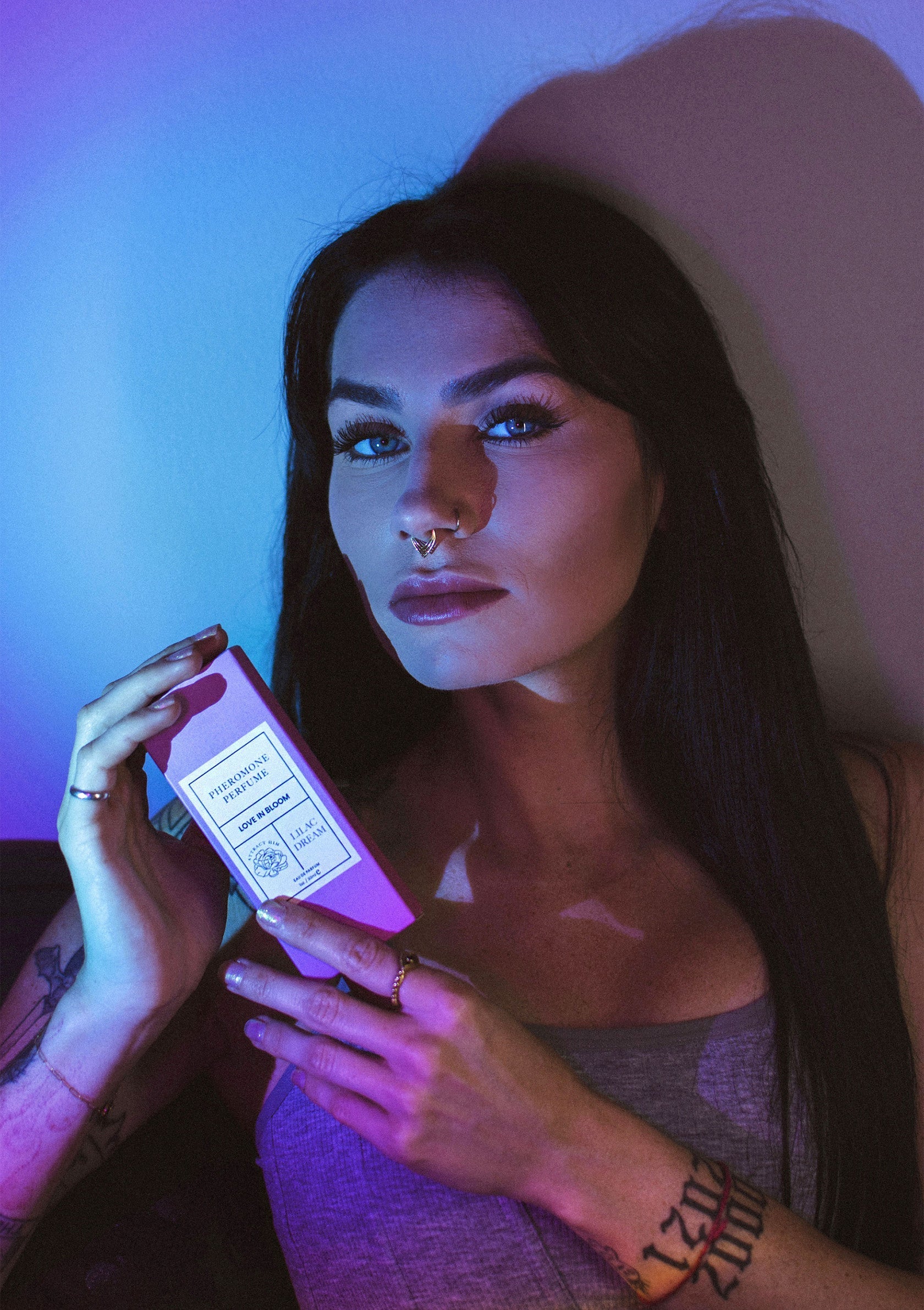 Femme tenant un produit de beauté luxueux sous un éclairage violet et bleu. Découvrez notre collection de soins de la peau.; Vrouw met luxe schoonheidsproduct in paarse en blauwe verlichting. Ontdek onze huidverzorgingscollectie.; Woman holding luxury beauty product in purple and blue lighting. Discover our skincare collection.