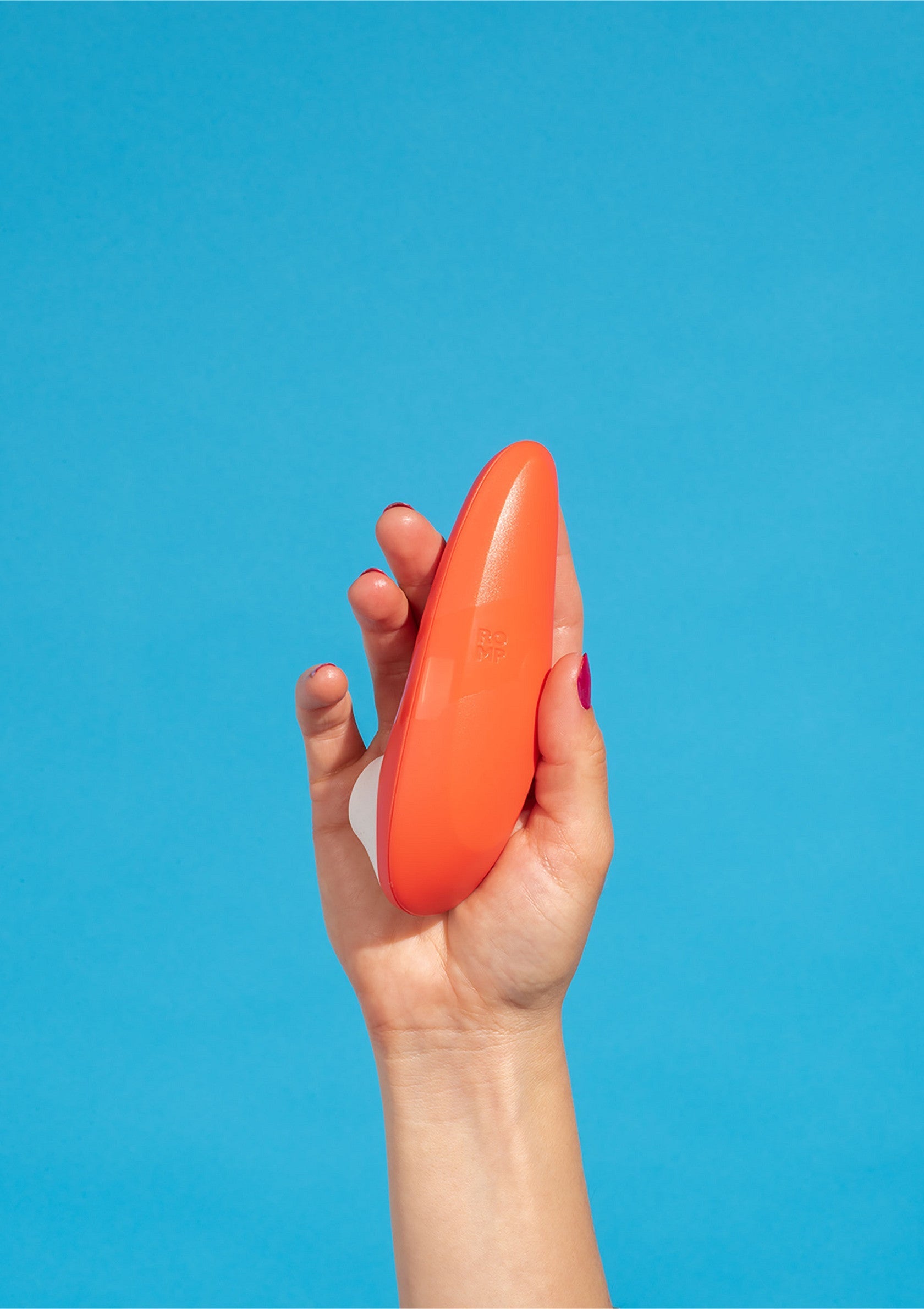 Masseur vibrant orange tenu à la main sur fond bleu. Plaisir et détente garantis!; Oranje vibrerende stimulator in hand tegen blauwe achtergrond. Plezier en ontspanning gegarandeerd!; Orange vibrating massager in hand against blue background. Pleasure and relaxation guaranteed!