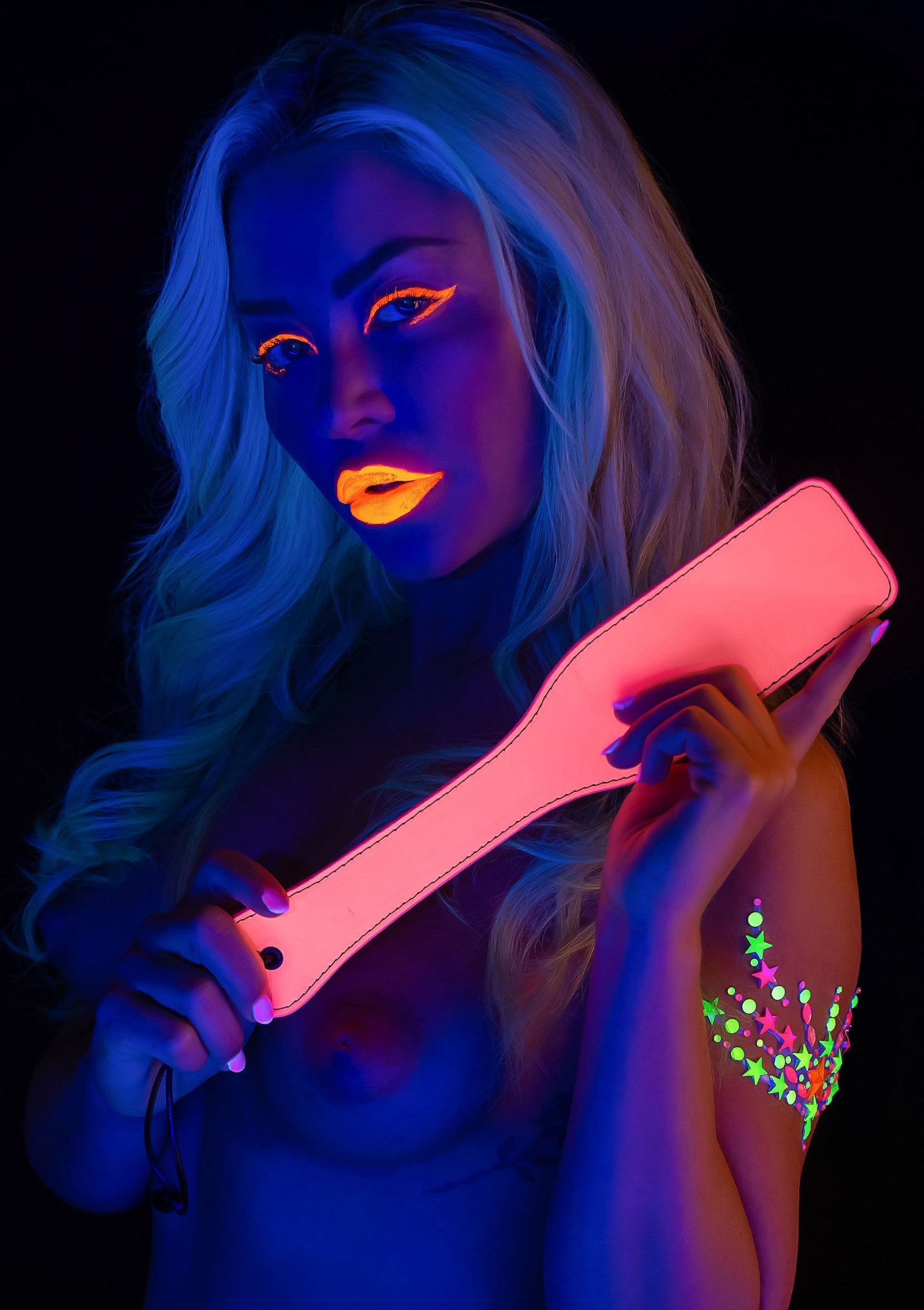 Femme séduisante avec un accessoire de badine fluo pour jeux coquins. Ajoutez une touche d'excitation à votre vie amoureuse !; Verleidelijke vrouw met neon spank paddle accessoire voor spannende spelletjes. Voeg een vleugje opwinding toe aan je liefdesleven!; Seductive woman with neon spank paddle accessory for exciting games. Add a touch of excitement to your love life!