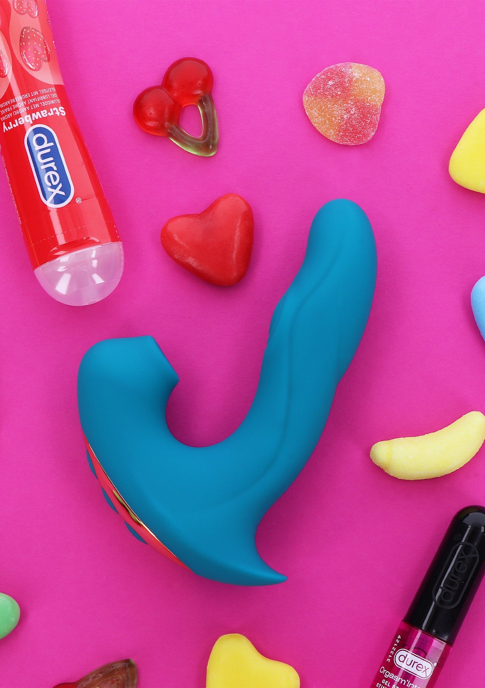 Vibromasseur bleu entouré de bonbons colorés et de lubrifiant Durex sur fond rose. Idéal pour pimenter votre vie amoureuse.; Blauwe vibrator omringd door kleurrijke snoepjes en Durex glijmiddel op een roze achtergrond. Ideaal om je liefdesleven op te fleuren.; Blue vibrator surrounded by colorful candy and Durex lubricant on a pink background. Ideal for spicing up your love life.