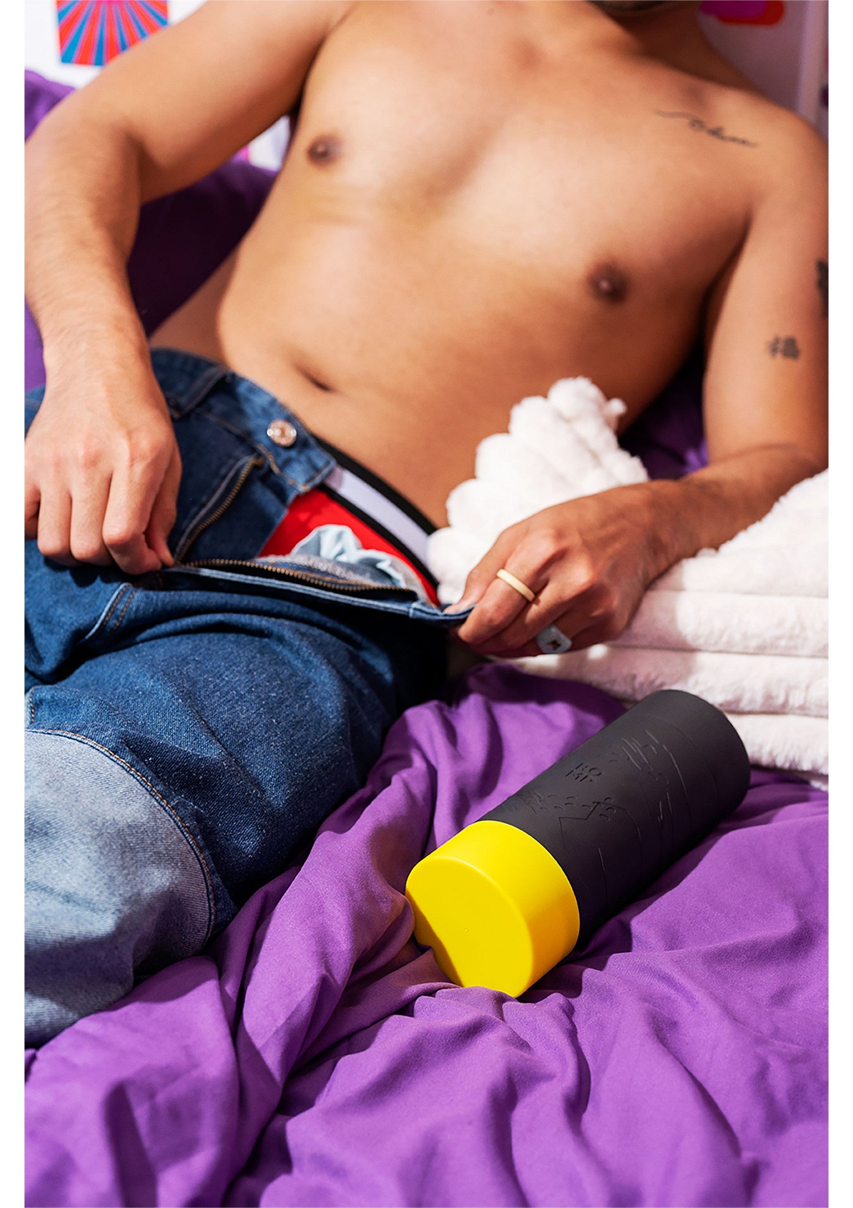 Un homme décontracté présente un sextoy cylindrique noir et jaune sur un lit violet.; Ontspannen man toont een zwarte en gele cilindervormige seksspeeltje op een paars bed.; Relaxed man showcasing a black and yellow cylindrical sex toy on a purple bed.