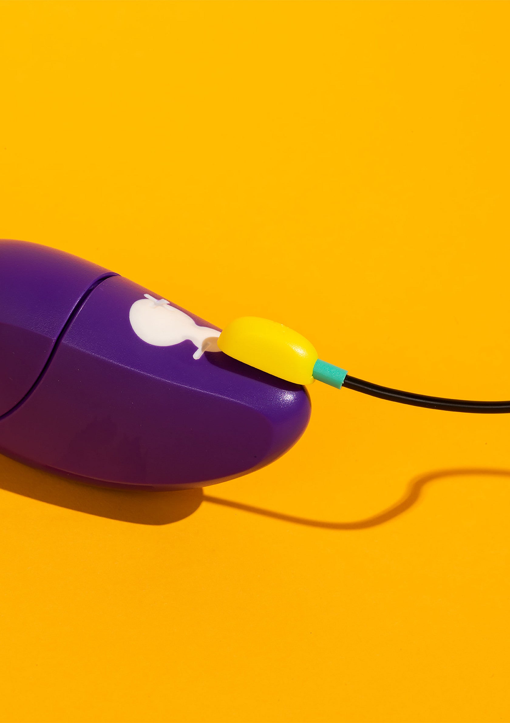 Jouet vibrant violet avec câble de charge jaune sur fond jaune.; Paars vibrerend speeltje met gele oplaadkabel op gele achtergrond.; Purple vibrator toy with yellow charging cable on yellow background.