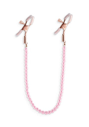 Pinces à tétons roses avec chaîne de perles pour un plaisir coquin et élégant.; Roze tepelklemmen met parelketting voor ondeugend en elegant genot.; Pink nipple clamps with pearl chain for naughty and elegant pleasure.