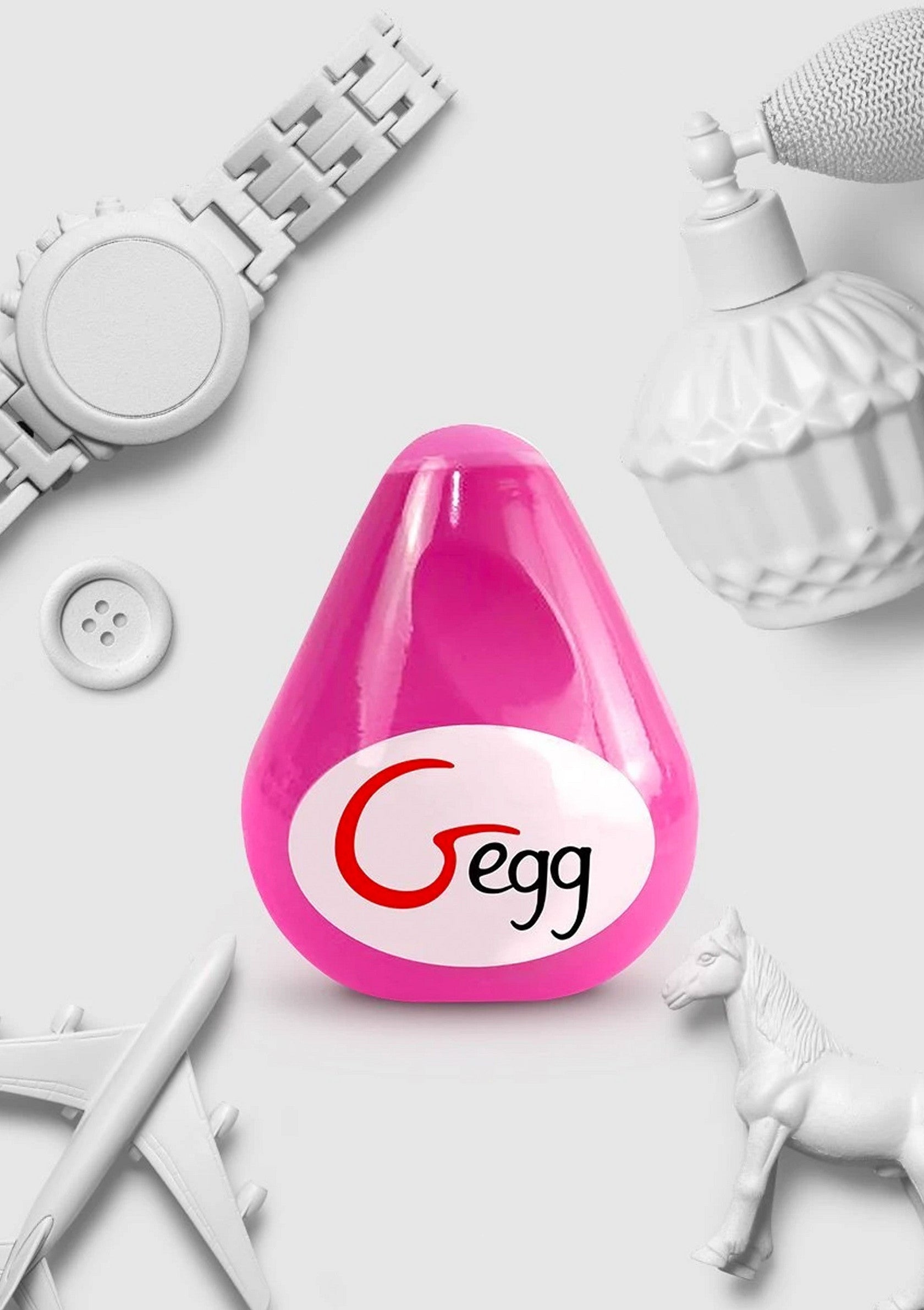 Image d'un produit rose 'Gegg' entouré d'accessoires blancs : montre, parfum, avion, cheval et bouton.; Afbeelding van een roze 'Gegg'-product omringd door witte accessoires: horloge, parfum, vliegtuig, paard en knoop.; Image of a pink 'Gegg' product surrounded by white accessories: watch, perfume, airplane, horse, and button.