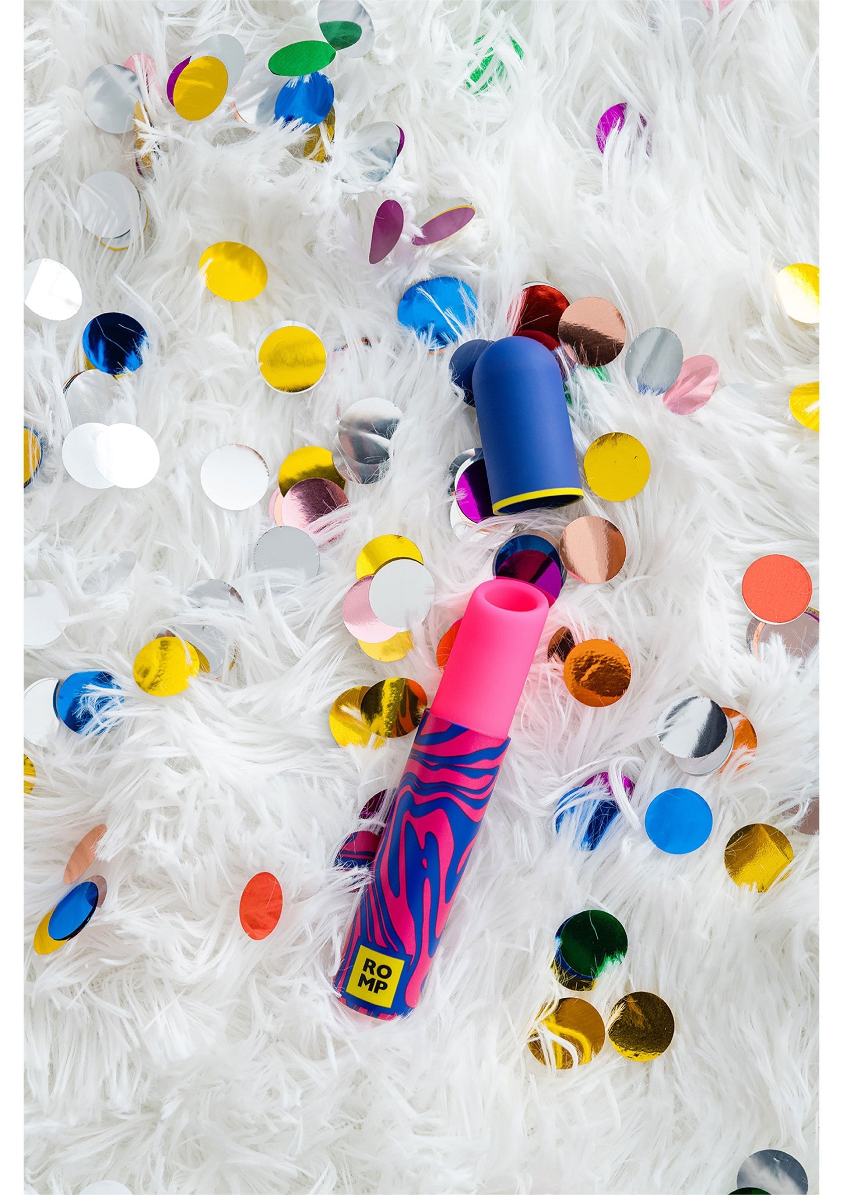 Vibromasseur ROMP coloré sur une couverture blanche avec des confettis pour une ambiance festive et ludique.; Kleurrijke ROMP vibrator op een witte deken met confetti voor een feestelijke en speelse sfeer.; Colorful ROMP vibrator on a white blanket with confetti for a festive, playful ambiance.