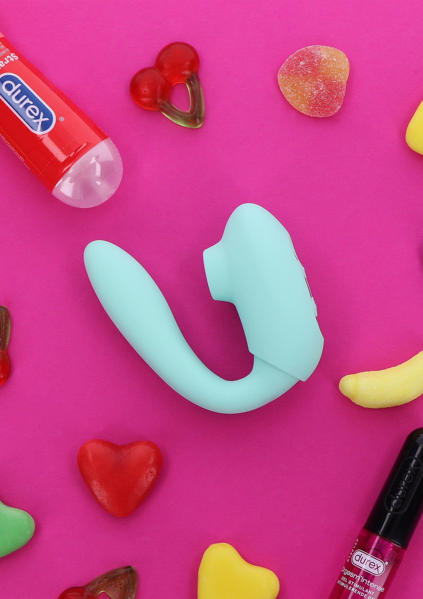 Vibromasseur turquoise ludique avec bonbons et préservatif sur fond rose.; Speelse turquoise vibrator met snoepjes en condoom op roze achtergrond.; Playful turquoise vibrator with sweets and condom on a pink background.