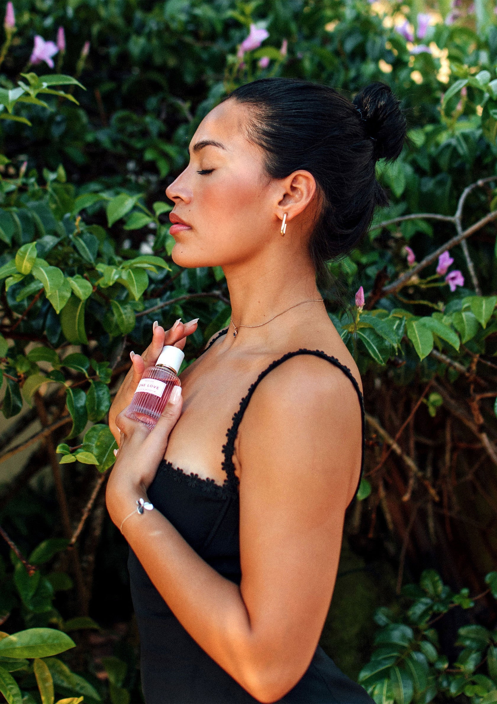 Femme élégante tenant un parfum devant un fond de verdure luxuriante. Collection de parfums.; Elegante vrouw houdt een parfum vast tegen een achtergrond van weelderig groen. Parfumcollectie.; Elegant woman holding perfume against a backdrop of lush greenery. Perfume collection.
