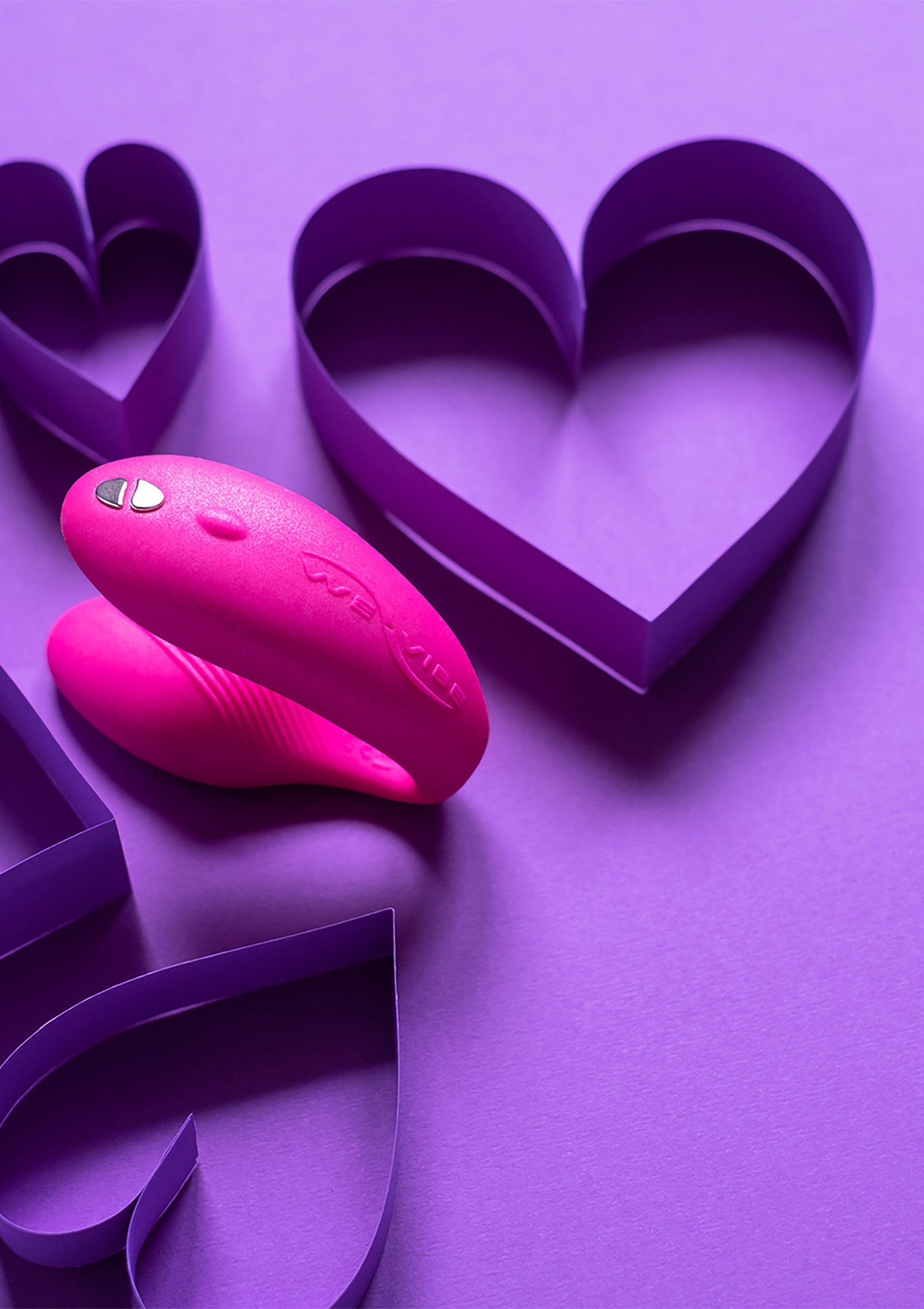 Vibromasseur rose avec coeurs violets pour la Saint-Valentin ou pour un moment de plaisir personnel.; Roze vibrator met paarse harten voor Valentijnsdag of een moment van persoonlijk genot.; Pink vibrator with purple paper hearts for Valentine's Day or a moment of personal pleasure.