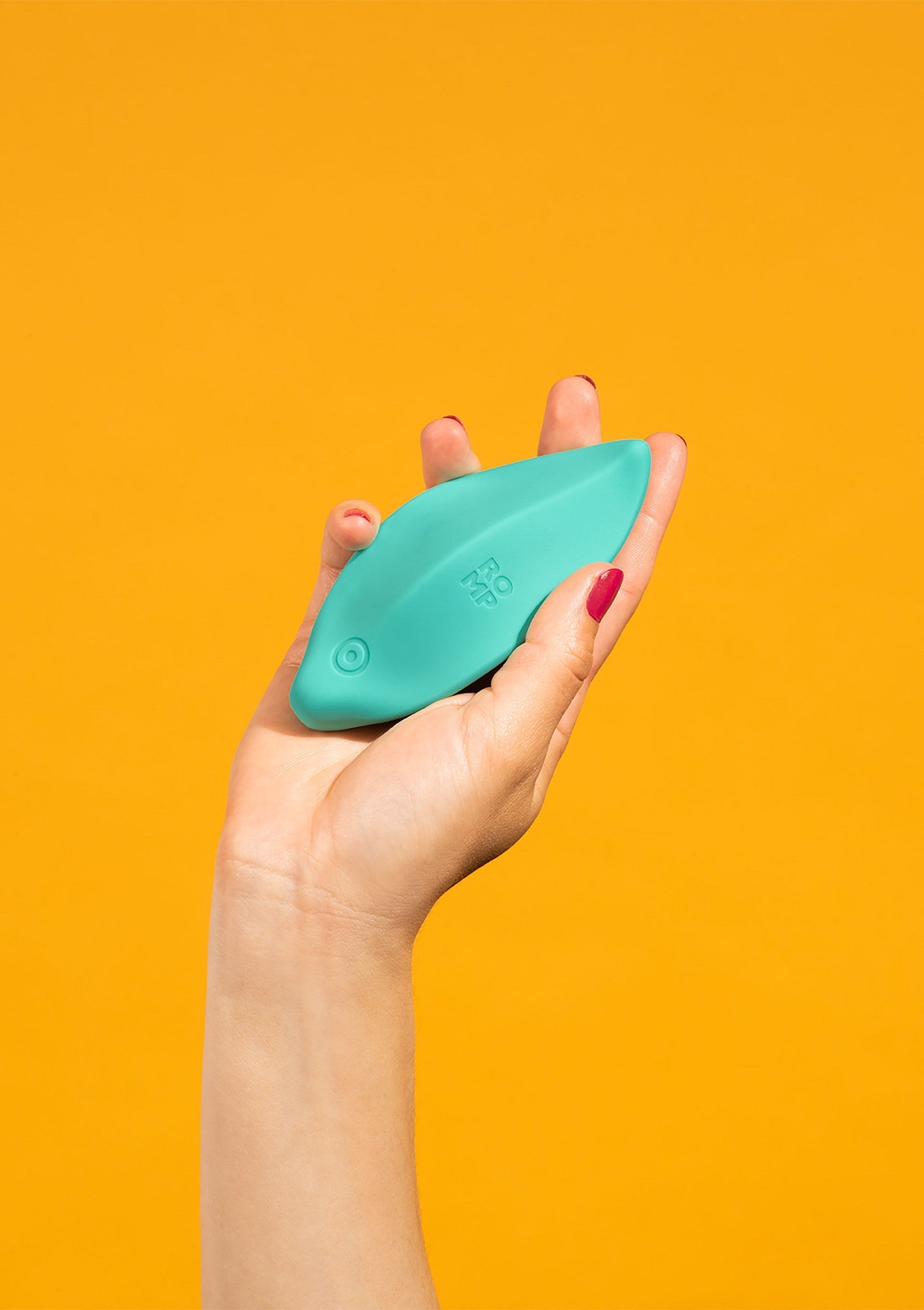 Masseur vibrant bleu turquoise dans la main d'une femme, sur fond orange. Bien-être et relaxation.; Turkooisblauwe vibrerende massager in de hand van een vrouw, tegen een oranje achtergrond. Welzijn en ontspanning.; Turquoise blue vibrating massager in a woman's hand, against an orange background. Well-being and relaxation.