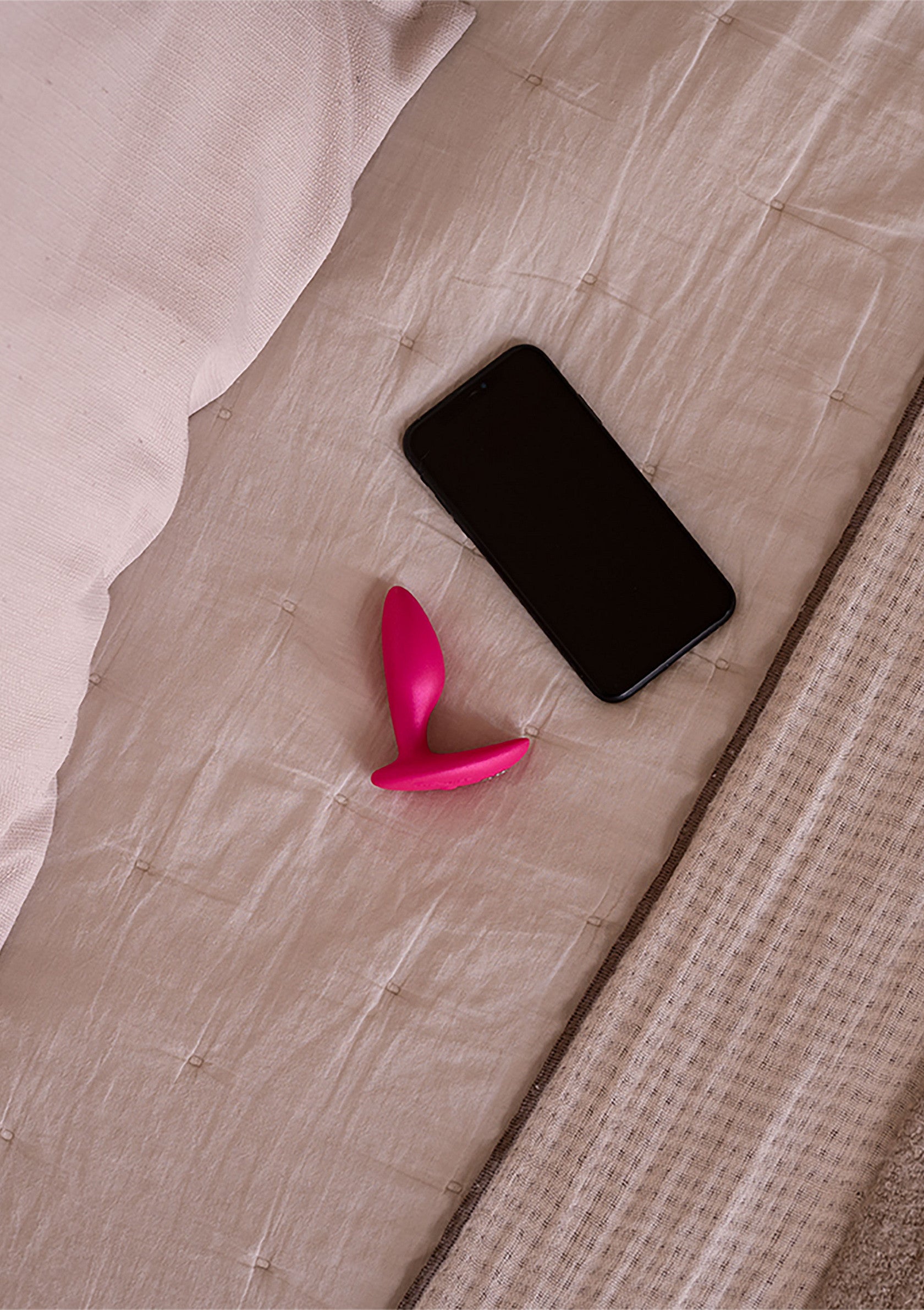 Gadget rose pour le plaisir avec téléphone sur lit confortable. Découvrez notre sélection d'accessoires intimes.; Roze speeltje met telefoon op een comfortabel bed. Bekijk onze selectie intieme accessoires.; Pink pleasure toy and phone on comfy bed. Explore our selection of intimate accessories.