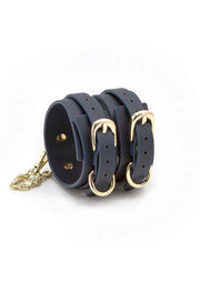 Manchette en cuir bleu marine à trois boucles dorées et chaîne décorative dorée.; Marineblauwe leren armband met drie gouden gespen en een decoratieve gouden ketting.; Navy leather cuff bracelet with three gold buckles and gold decorative chain.