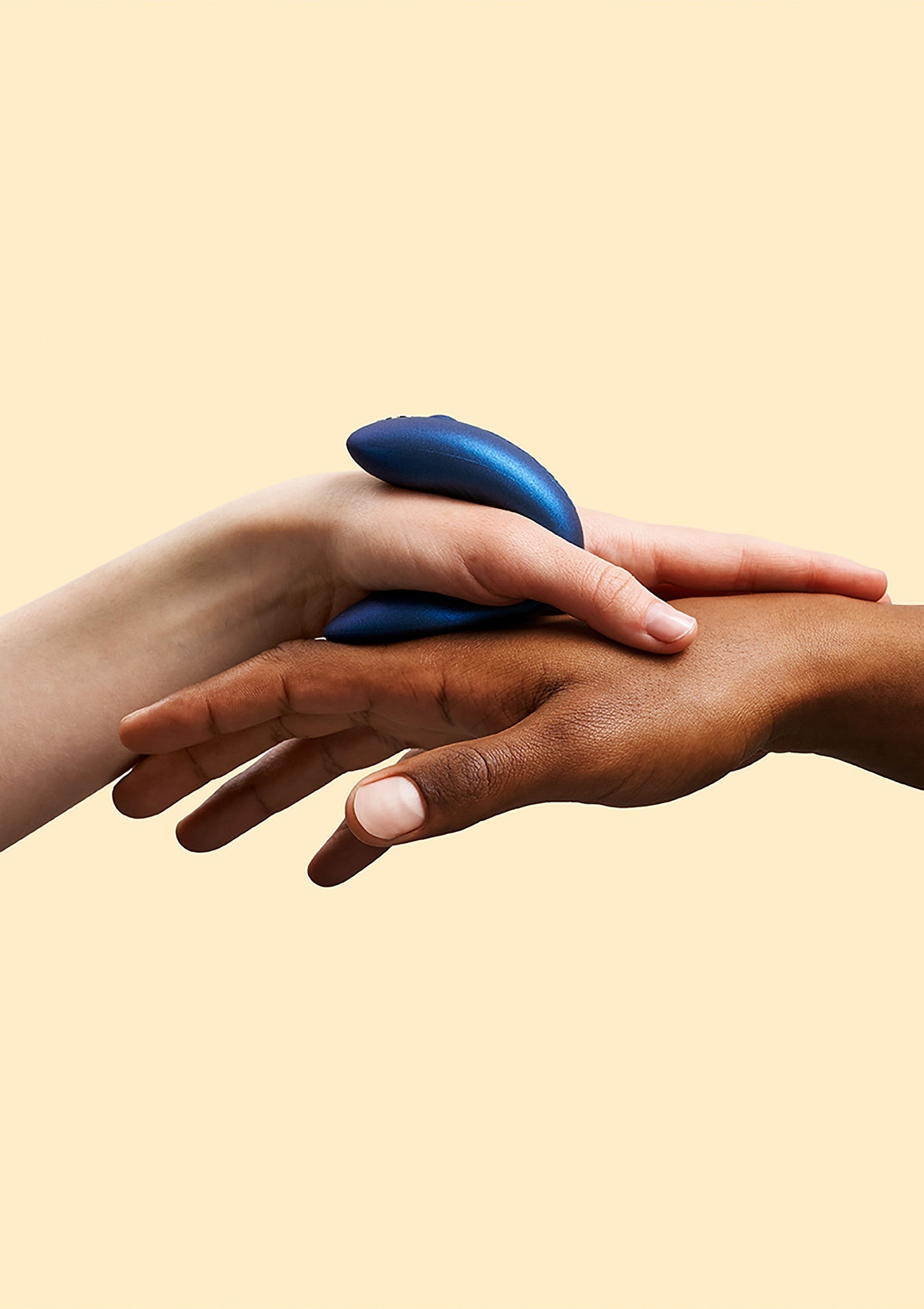 Vibrateur bleu posé sur deux mains de couleurs différentes pour une expérience partagée.; Blauwe vibrator rust op twee handen van verschillende kleuren voor een gedeelde ervaring.; Blue vibrator rests on two hands of different colors for a shared experience.
