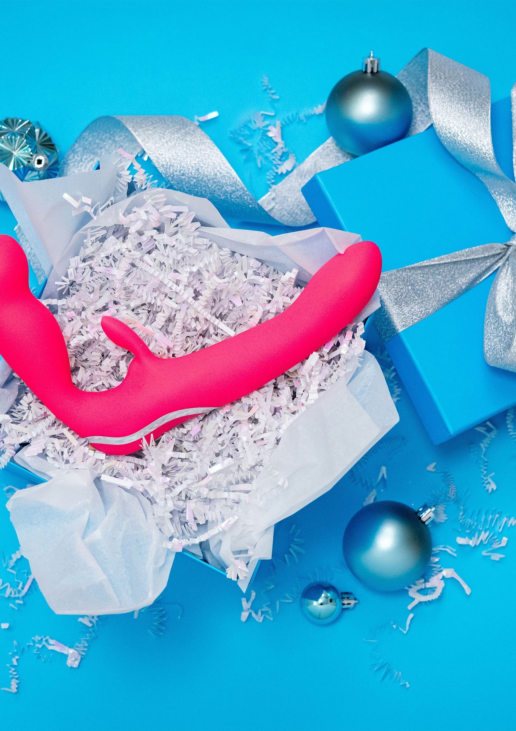 Cadeau coquin de Noël. Vibromasseur rose dans une boîte cadeau sur fond bleu festif.; Stoute kerstcadeau. Roze vibrator in geschenkdoos op feestelijke blauwe achtergrond.; Naughty Christmas gift. Pink vibrator in gift box on festive blue background.