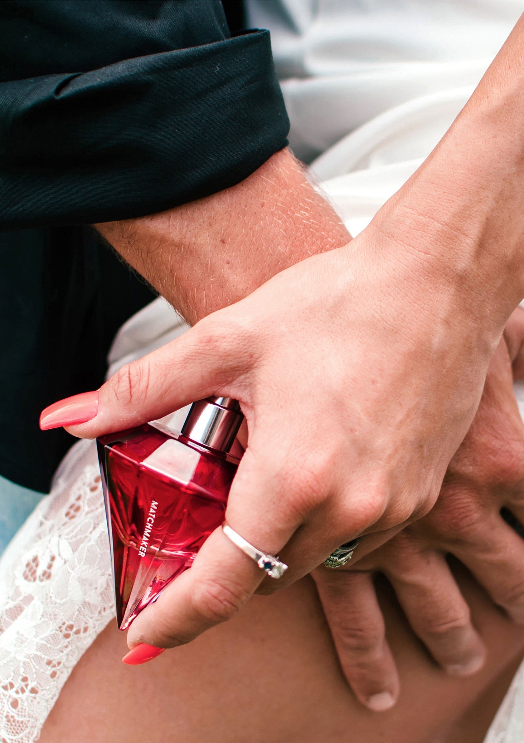 Flacon de parfum rouge Matchmaker tenu dans une main ornée d'une bague de fiançailles.; Rode Matchmaker parfumfles in de hand met verlovingsring. Romantisch cadeau-idee.; Red Matchmaker perfume bottle held in hand with engagement ring. Romantic gift idea.