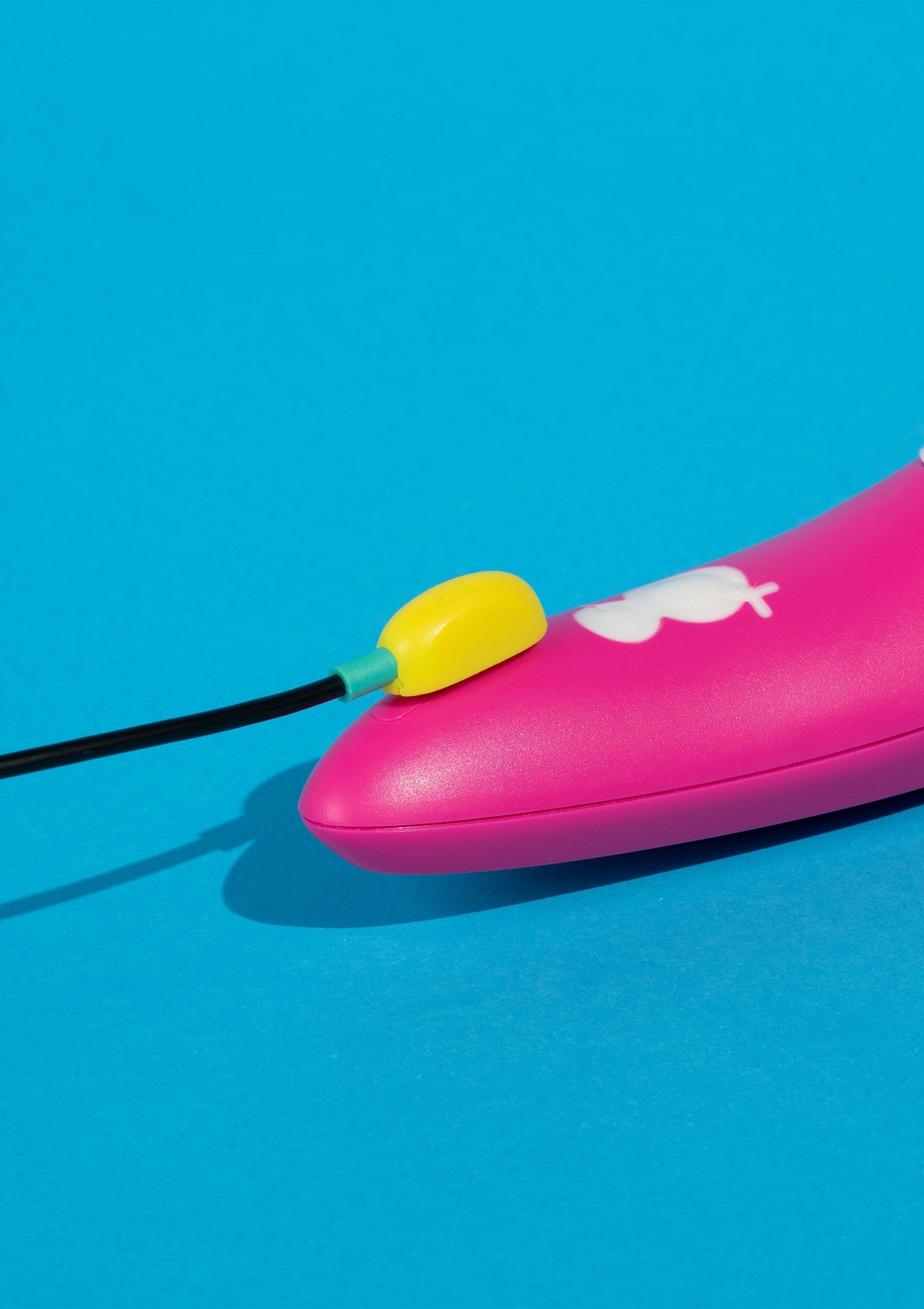 Gadget rose avec un câble noir et un connecteur jaune sur fond bleu vif.; Roze gadget met zwarte kabel en gele connector op helderblauwe achtergrond.; Pink gadget with black cable and yellow connector on a bright blue background.