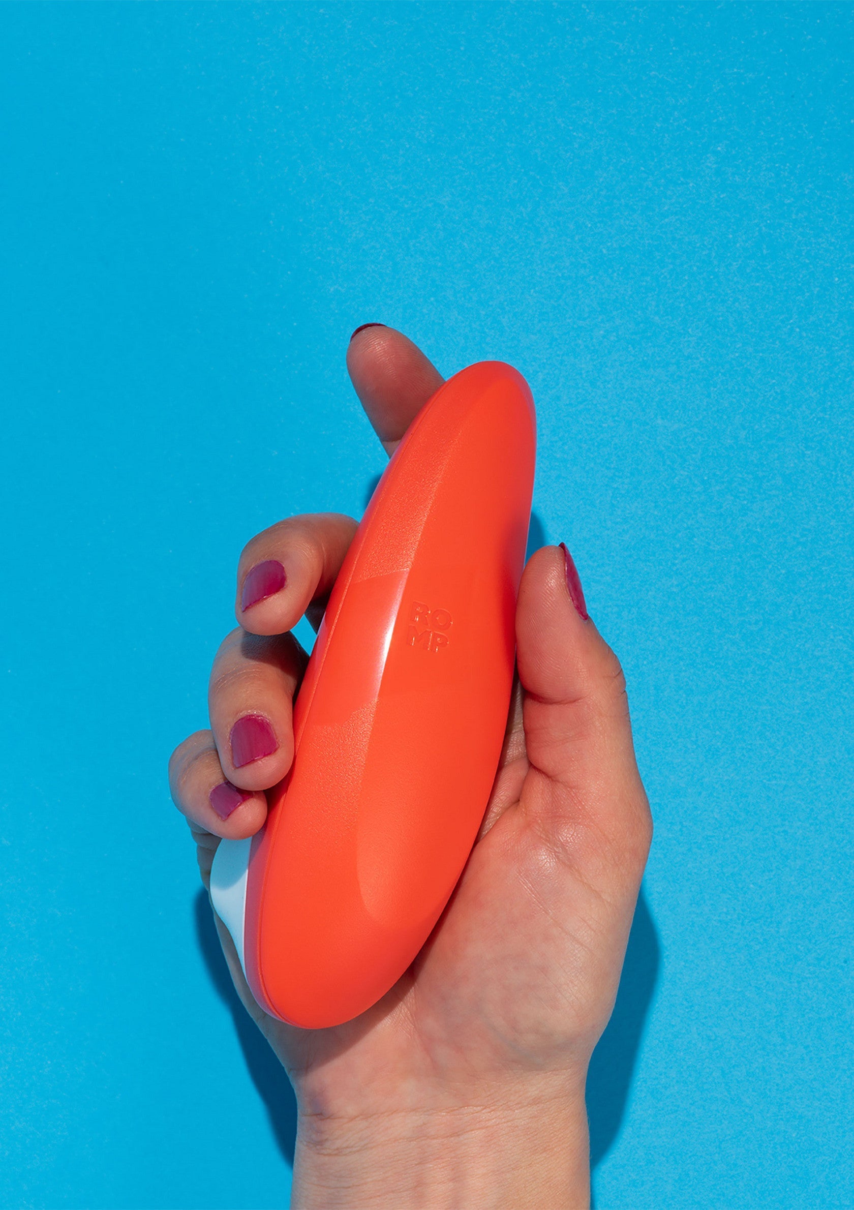 Masseur vibrant orange vif dans la main d'une femme sur fond bleu. Découvrez le plaisir ultime !; Fel oranje vibrerende massageapparaat in de hand van een vrouw tegen een blauwe achtergrond. Ontdek ultiem plezier!; Bright orange vibrating massager in a woman's hand against a blue backdrop. Discover ultimate pleasure!
