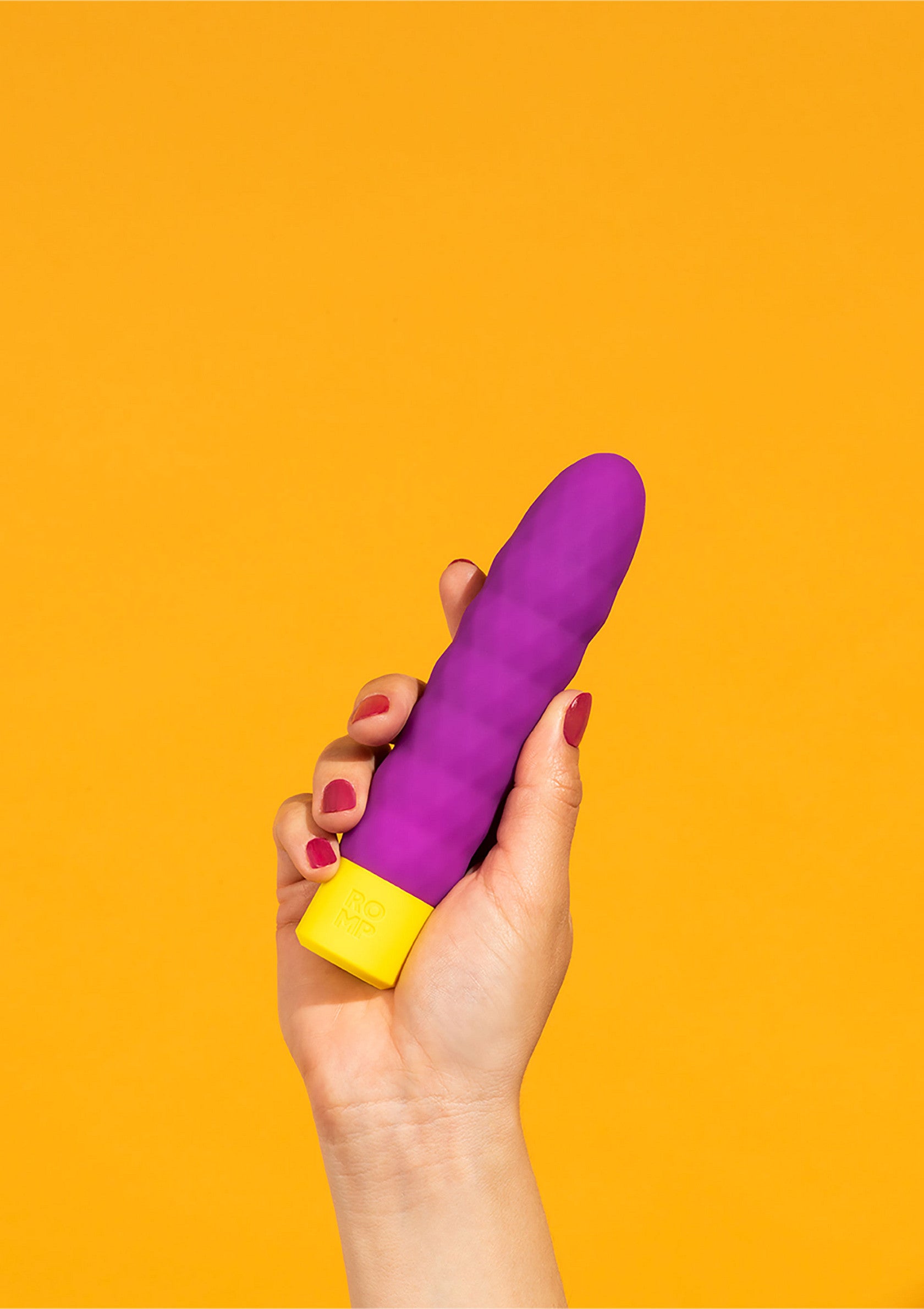 Vibromasseur violet et jaune dans une main sur fond orange. Plaisir, relaxation et bien-être garantis. Découvrez notre collection !; Paarse en gele vibrator in een hand tegen een oranje achtergrond. Plezier, ontspanning en welzijn gegarandeerd. Bekijk onze collectie!; Purple and yellow vibrator in hand on orange background. Pleasure, relaxation, and well-being guaranteed. Shop our collection now!