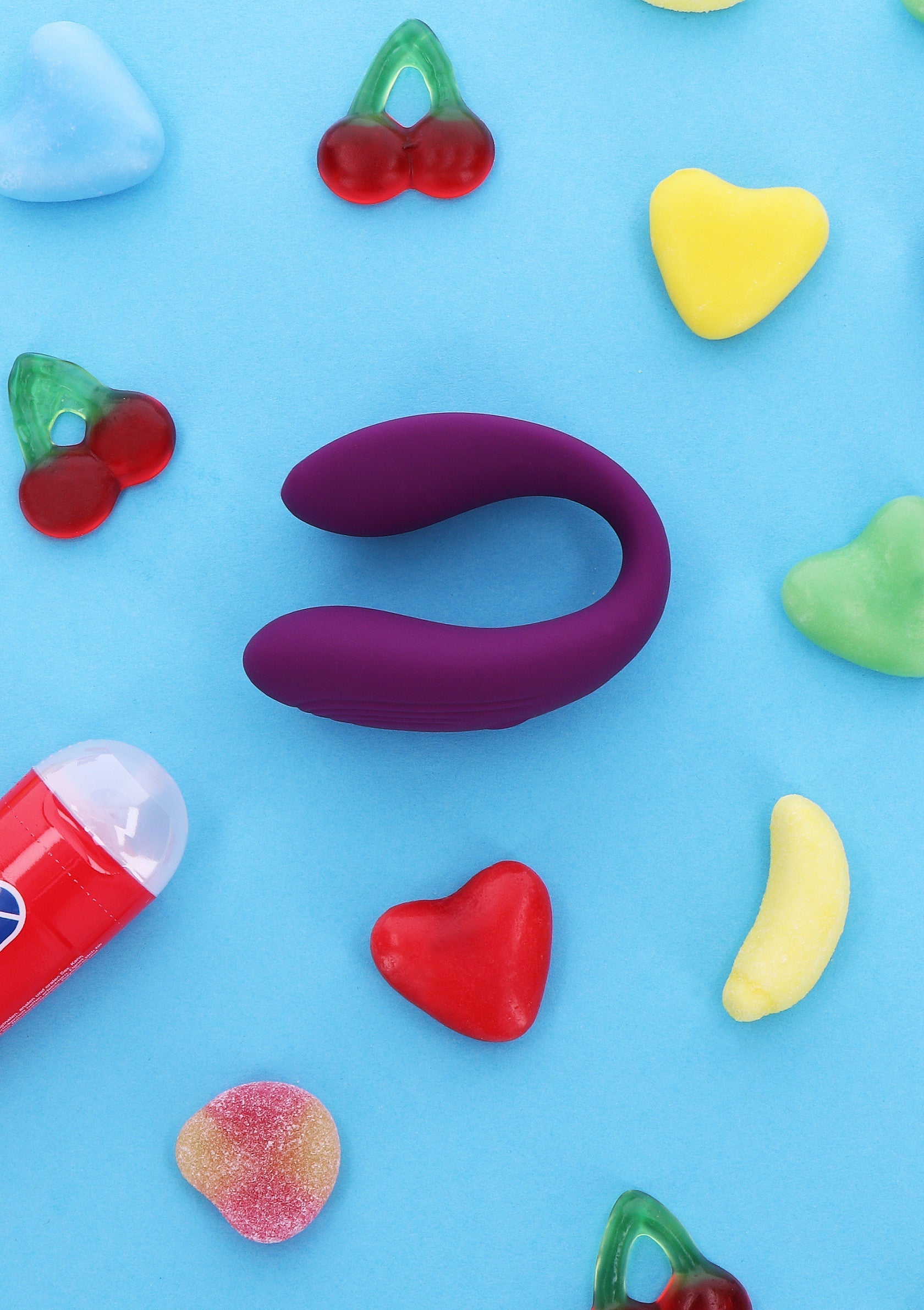 Vibromasseur violet avec bonbons colorés sur fond bleu. Amusez-vous et explorez !; Paarse vibrator met kleurrijke snoepjes op een blauwe achtergrond. Plezier en ontdek!; Purple vibrator with colorful candy on a blue background. Fun and explore!