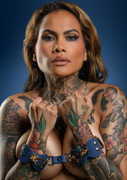 Menottes en cuir bleu avec une femme tatouée pour un jeu coquin.; Blauwe lederen handboeien op getatoeëerde vrouw voor ondeugend spel.; Blue leather handcuffs on tattooed woman for kinky play.
