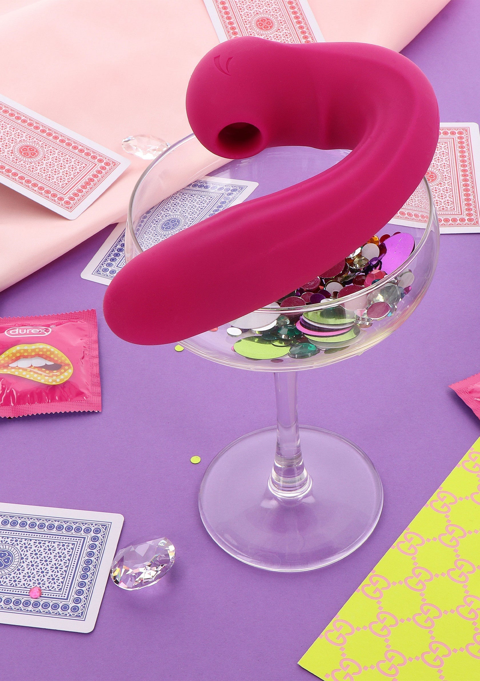 Vibromasseur rose sur verre à cocktail rempli de confettis, ambiance festive et ludique.; Roze vibrator op cocktailglas gevuld met confetti, een feestelijke en speelse sfeer.; Pink vibrator on cocktail glass filled with confetti, a festive and playful atmosphere.