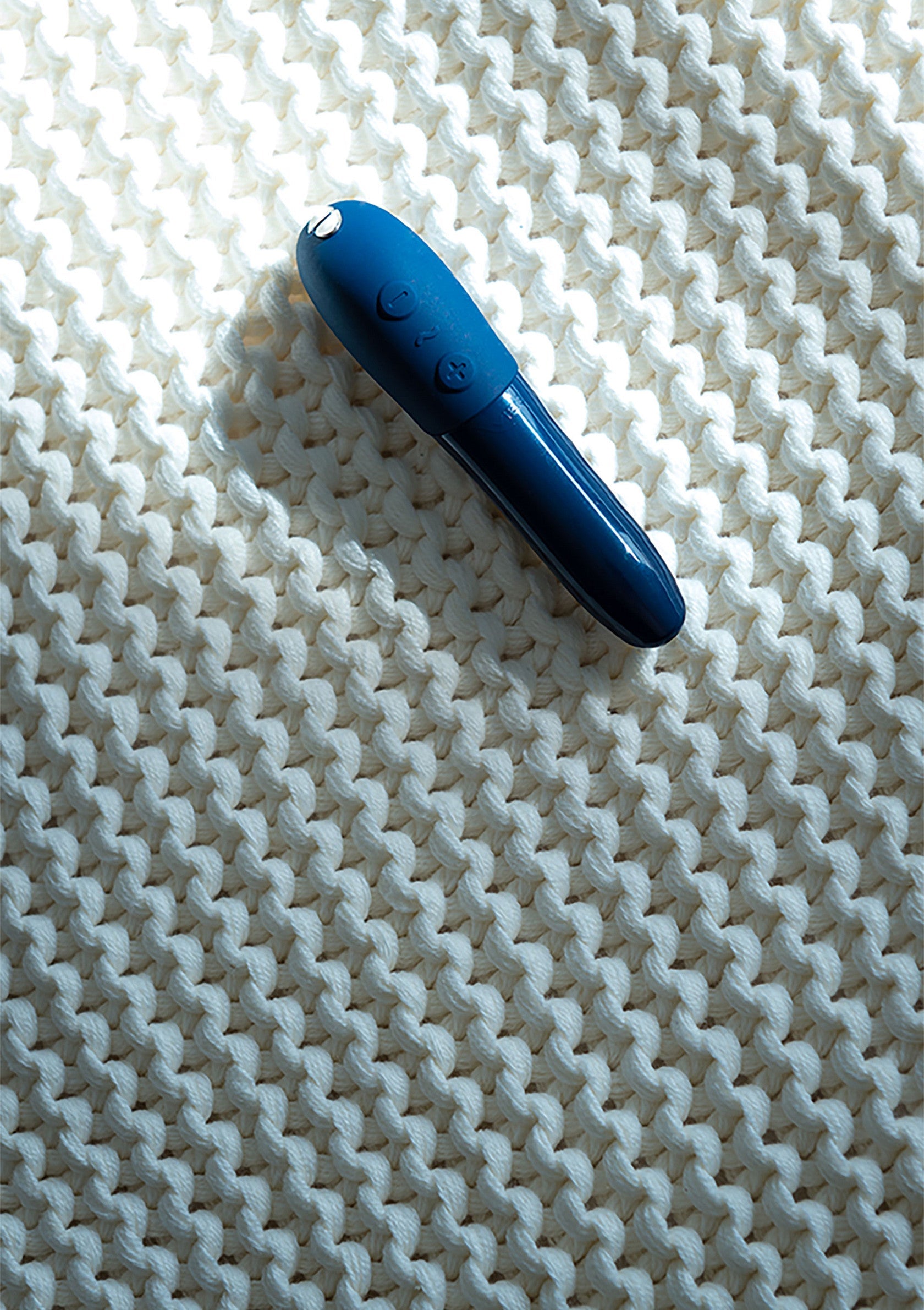 Masseur vibrant bleu sur fond de tricot blanc. Découvrez nos jouets intimes pour le plaisir !; Blauwe vibrerende stimulator op witte gebreide achtergrond. Ontdek ons intiem speelgoed voor plezier!; Blue vibrating massager on white knitted background. Discover our intimate toys for pleasure!